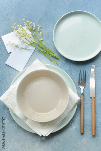 Beautiful table setting with lily-of-the-valley flowers on color background © Pixel-Shot