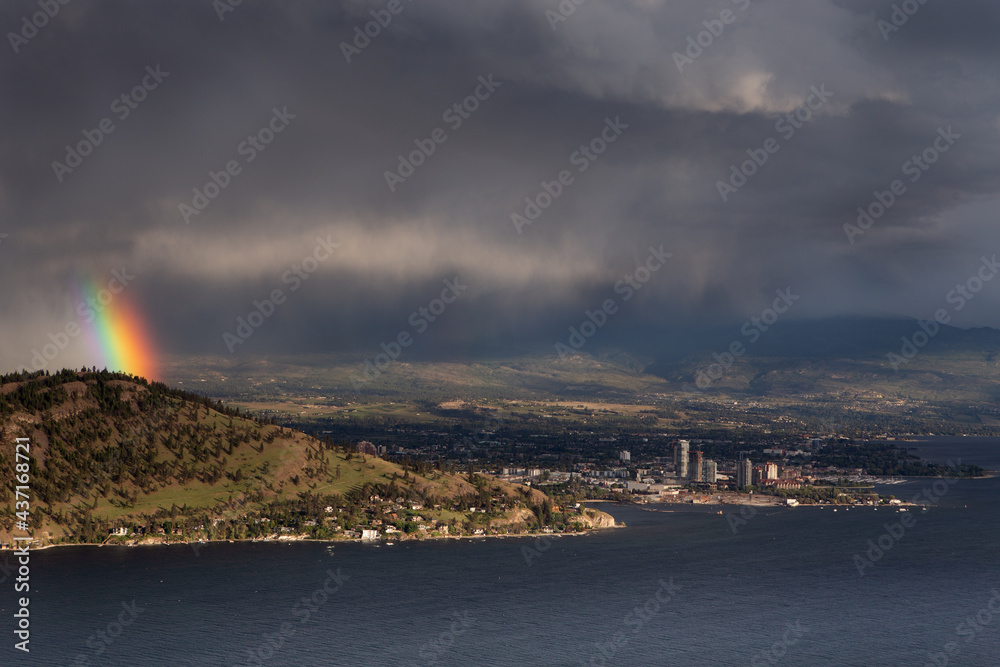 View of Kelowna with rainbow over the town, city. Landscape with rainbow over the city on a dark cloud background.