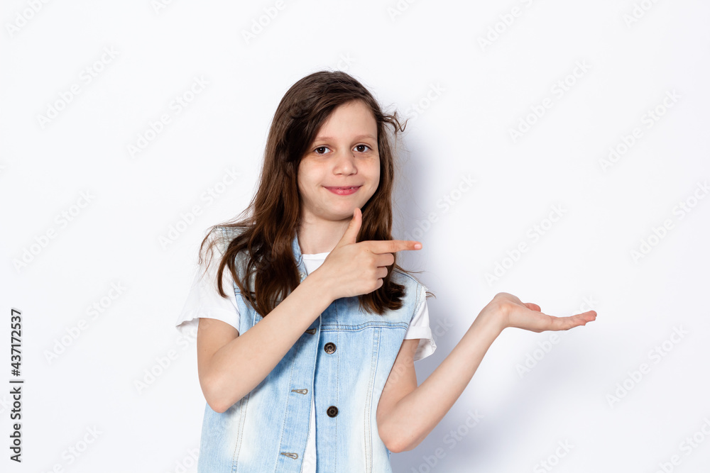 Funny dark-haired teen girl shows gesture with her hands on the wall. Portrait. On a light background. Place for your text. Funny dark-haired teen girl shows gesture with her hands on the wall. Portrait. On a light background. Place for your text.
