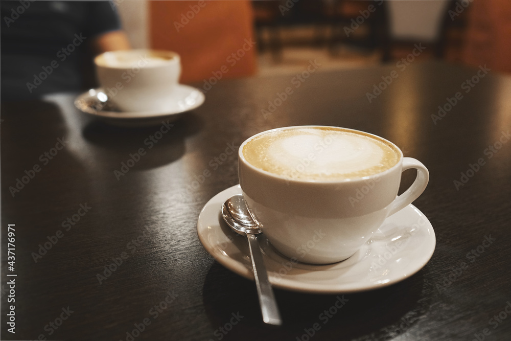 a white cappuccino coffee cup with a heart - shaped pattern on the foam. a cup and saucer on a dark wooden table in a cafe or restaurant a white cappuccino coffee cup with a heart - shaped pattern on the foam. a cup and saucer on a dark wooden table in a cafe or restaurant
