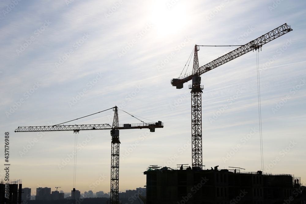 Silhouette of construction crane and workers on unfinished residential building against sunshine. Housing construction, apartment block in city