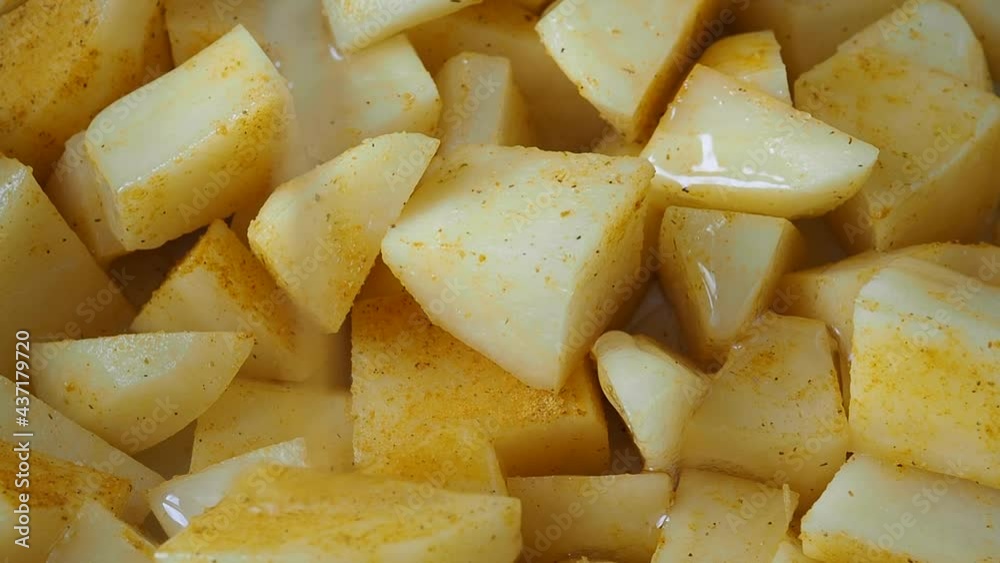 Raw potato slices in a ceramic baking tray with spices are poured with vegetable oil. Raw potato slices in a ceramic baking tray with spices are poured with vegetable oil.