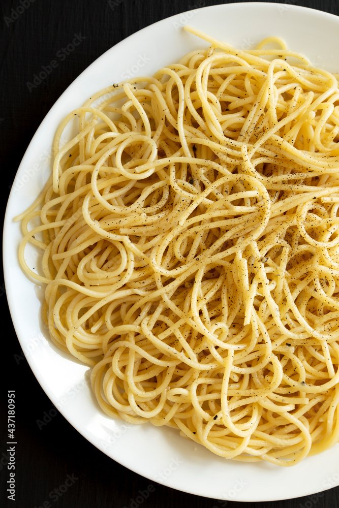 Homemade Cacio E Pepe Pasta with Pecorino Romano and Pepper on a white plate on a black surface, top view. Overhead, from above. Homemade Cacio E Pepe Pasta with Pecorino Romano and Pepper on a white plate on a black surface, top view. Overhead, from above.