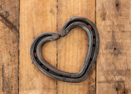 Romantic love heart shaped horse shoe created by farrier laid on rustic vintage wooden plank background.
