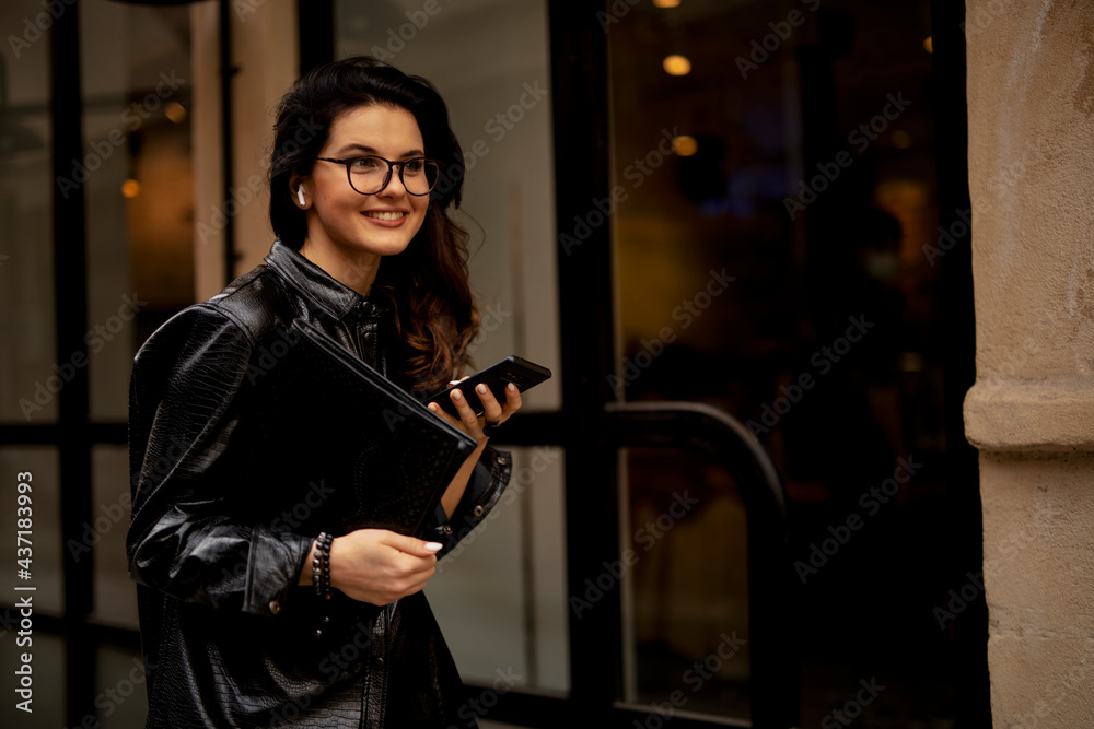 Young smiling woman enjoying outdoors. Beautiful woman using the phone while walking in the morning....
