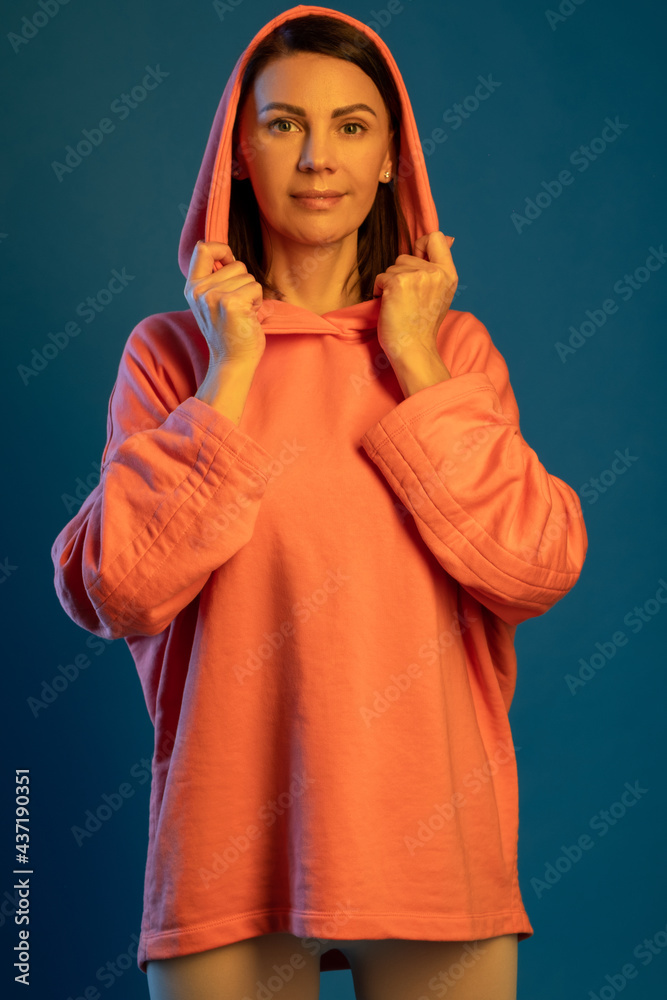 Smiling woman in hooded sweatshirt looking at camera against blue background Smiling woman in hooded sweatshirt looking at camera against blue background