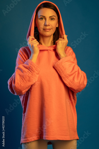 Smiling woman in hooded sweatshirt looking at camera against blue background © nazarovsergey