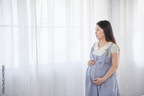 Young Asian pregnant smiling and holding her tummy anticipating to see her baby in a few days.