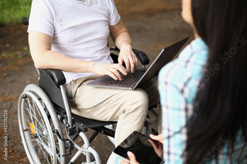 Man in wheelchair works on laptop on street next to woman sits and holds tablet