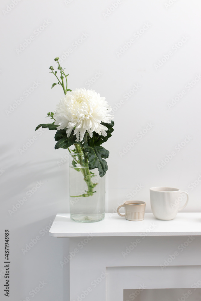 A large chrysanthemum in a glass vase, two fluted cups of coffee and ceramic bird figurines on the table. Office decoration. A large chrysanthemum in a glass vase, two fluted cups of coffee and ceramic bird figurines on the table. Office decoration.