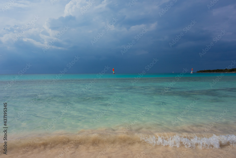 storm clouds approaching beach with waves and blue sea and sails in the distance