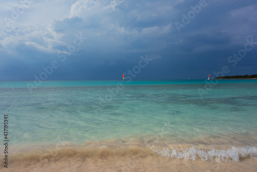 storm clouds approaching beach with waves and blue sea and sails in the distance
