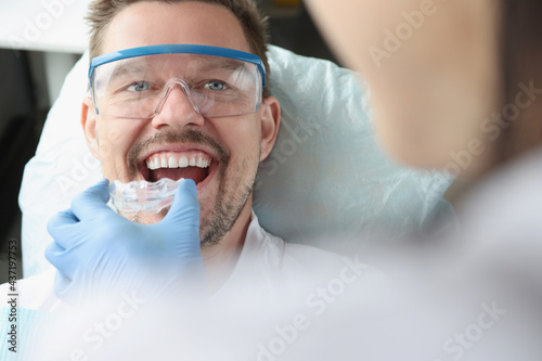 Doctor tries on plastic mouthguard for young smiling man to correct bite