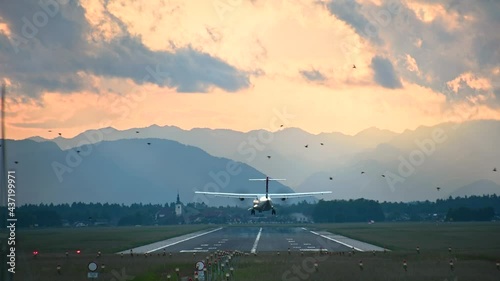 Old passenger airplane landing on the runway against beautiful dramatic sunset at Brnik airport, Slovenia. Aircraft landing. View of long runway and Alps mountains photo