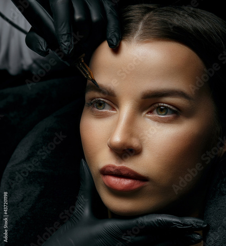 Attractive brunette woman having eyebrow tattoo procedure