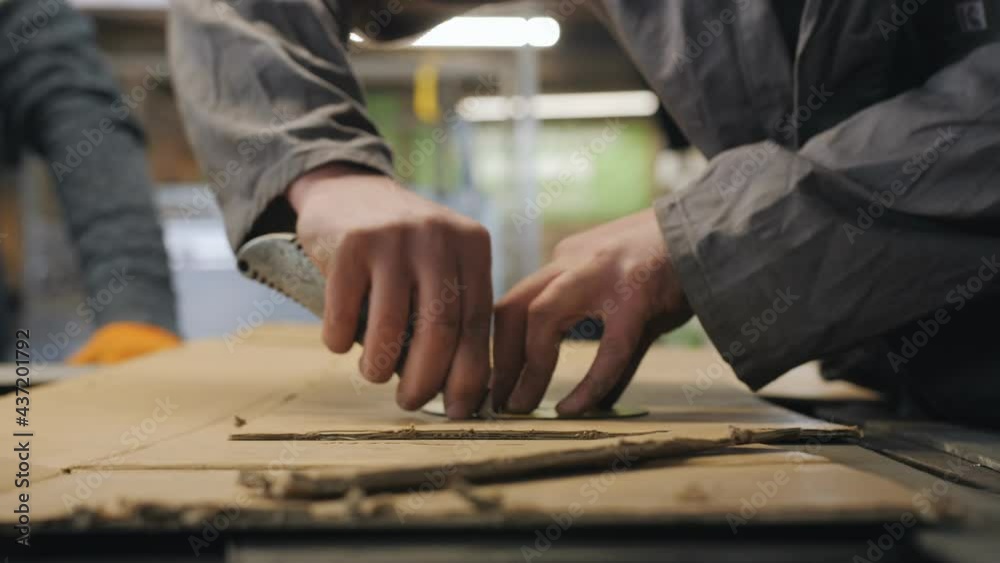 Close-up of the hands of an auto mechanic cutting out a cardboard blank with a knife on the desktop in an auto repair shop. Close-up of the hands of an auto mechanic cutting out a cardboard blank with a knife on the desktop in an auto repair shop.