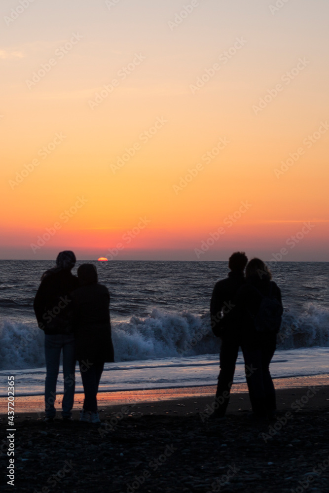 Couple in love watching sunset together on beach travel summer holidays. People silhouette from behind sitting enjoying view sunset sea on tropical destination vacation.