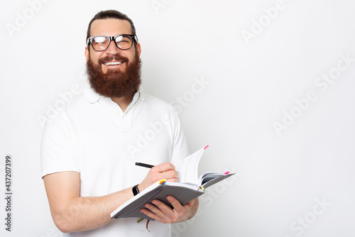 Happy smiling man with beard making notes in his agenda or planner