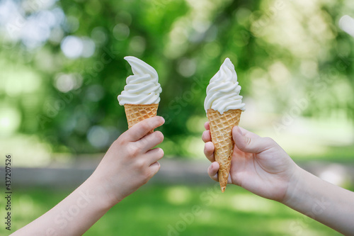 Two cones with creamy ice cream in children's hands. Children walk in the park in summer and eat sweets. Horizontal photo with place for text.