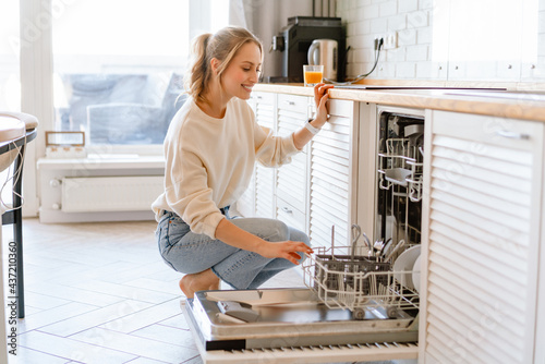 Smiling young white woman putting dishes in the dishwasher at home photo