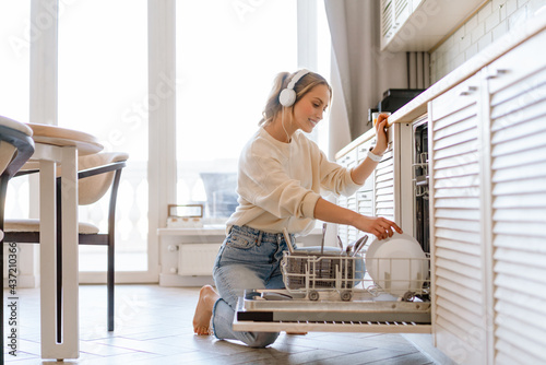Fotografía Smiling young white woman putting dishes in the dishwasher at home