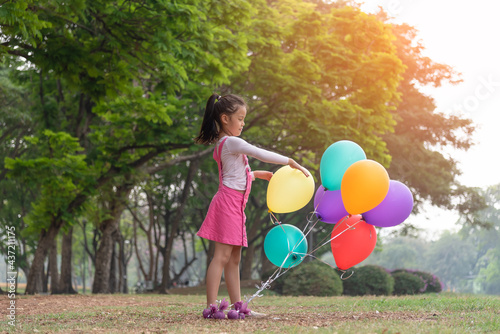 Little lovely girl holding a colorful balloons smiling in the park. Girls has a happy holiday.