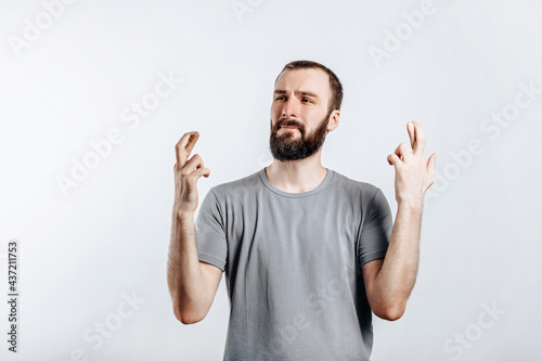 Handsome young man frown and cross fingers in hope on white background with space for advertising mock up