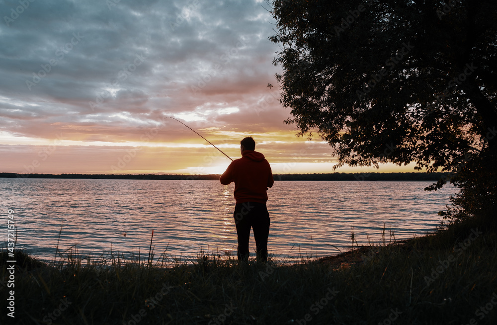 One fisherman is fishing at sunset on a large beautiful lake.