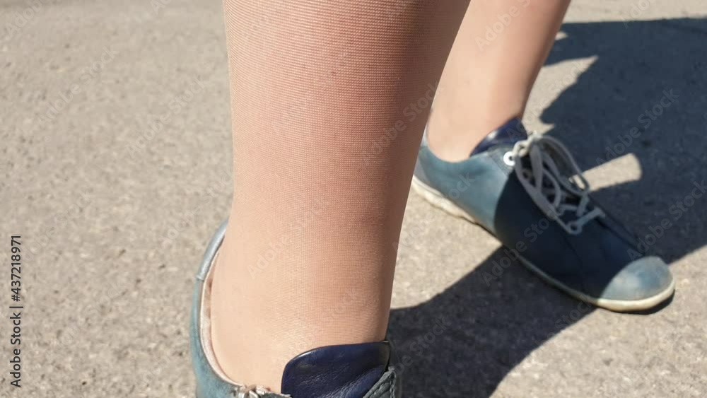women's legs in shiny beige tights, pantyhose with sneakers
