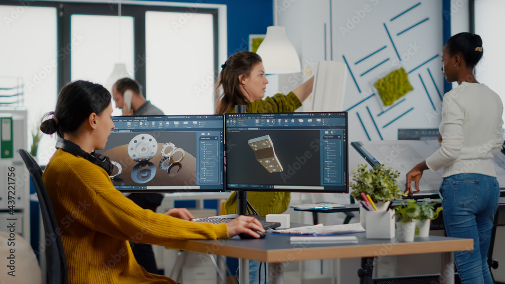 Industrial female engineer looking at personal computer with dual monitors setup, screens showing CAD software with 3D prototype of gears metalic mechanical piece. Employee working in creative office Industrial female engineer looking at personal computer with dual monitors setup, screens showing CAD software with 3D prototype of gears metalic mechanical piece. Employee working in creative office