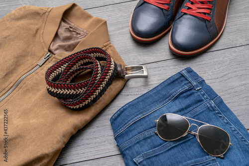 Set of stylish male clothes with shoes , belt, jacket, jeans, sunglasses on wooden background. Flat lay