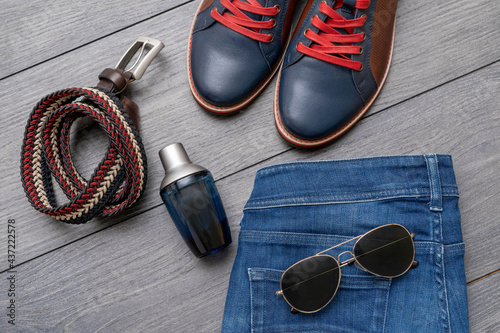 Set of stylish male clothes with shoes, belt, jeans, sunglasses, perfume on wooden background. Flat lay