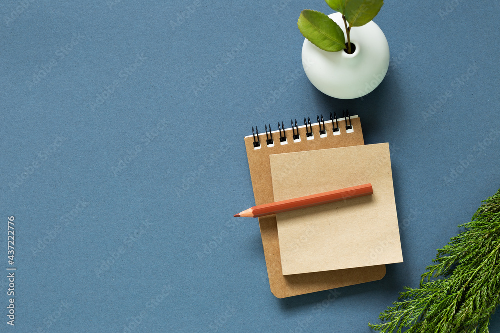Notebook and colored pencil and vase of plant on desk. navy blue background. flat lay, top view, copy space
