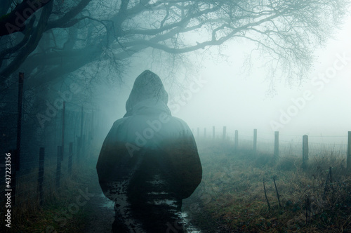 A double exposure of an atmospheric half transparent man looking at a foggy path in the countryside. On a moody foggy winters day.