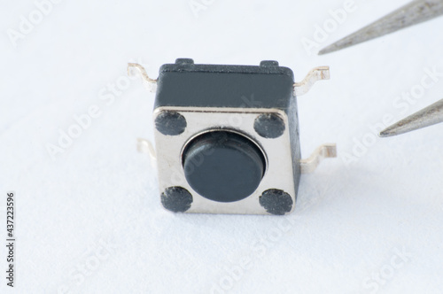 Marco of Tactile button switch. Pick up a TACT switch component with a pair of tweezers. Surface Mount Device. photo