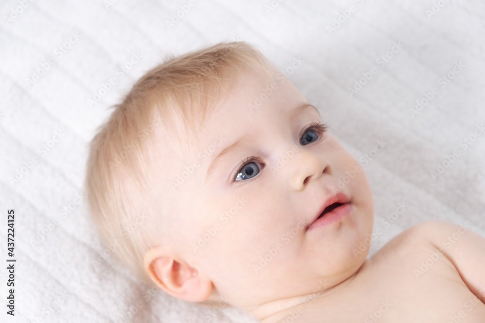 Beautiful caucasian blonde baby girl, infant lying on bed. Happy childhood, baby care concept, close-up Beautiful caucasian blonde baby girl, infant lying on bed. Happy childhood, baby care concept, close-up