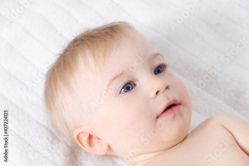 Beautiful caucasian blonde baby girl, infant lying on bed. Happy childhood, baby care concept, close-up