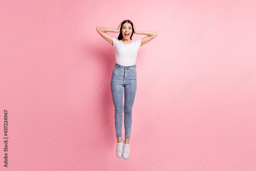 Full size photo of impressed brunette lady jump wear white t-shirt jeans sneakers isolated on pastel pink color background Full size photo of impressed brunette lady jump wear white t-shirt jeans sneakers isolated on pastel pink color background