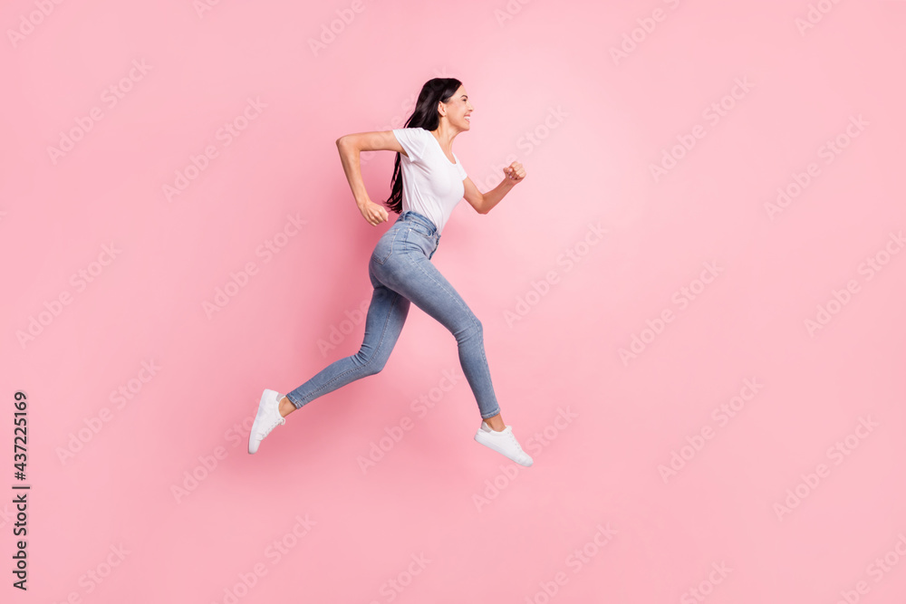 Full size profile photo of optimistic brunette lady jump go wear t-shirt jeans sneakers isolated on pastel pink color background Full size profile photo of optimistic brunette lady jump go wear t-shirt jeans sneakers isolated on pastel pink color background