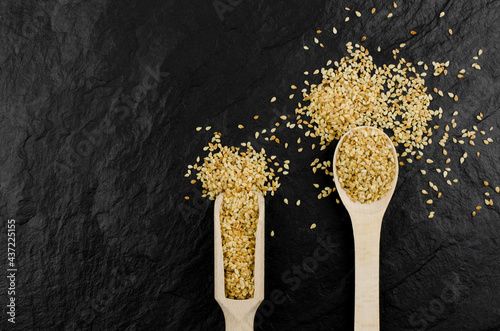 Flax seeds in wooden spoons on a black stone background.
