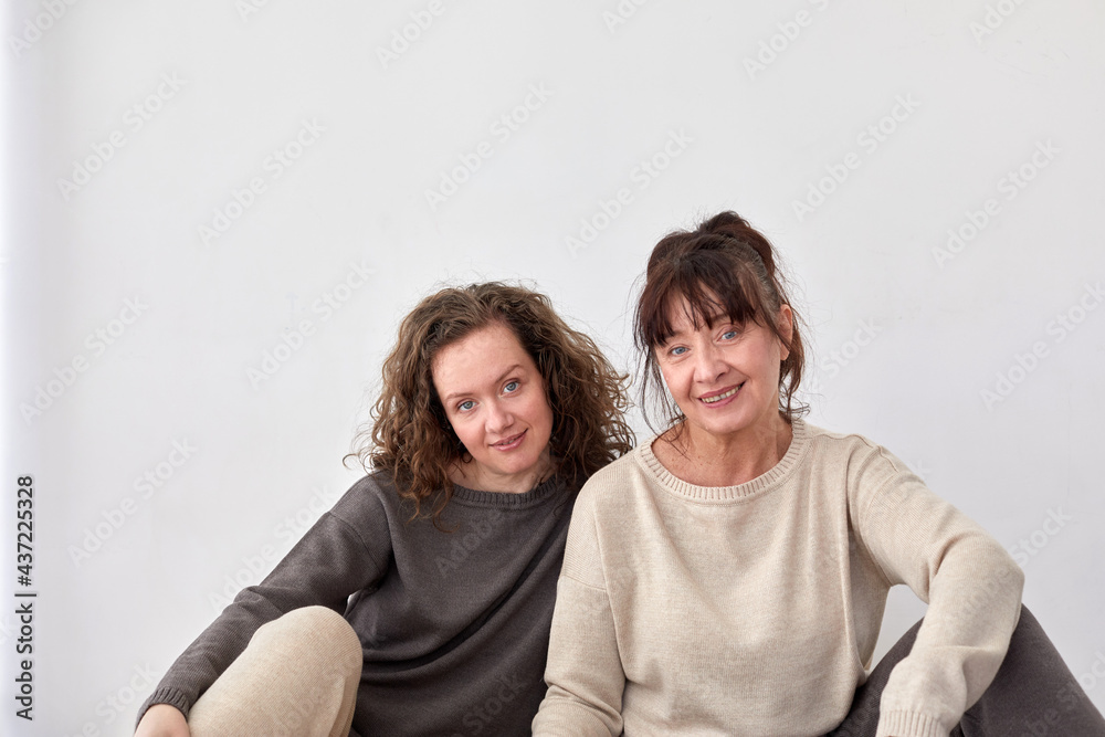 Cheerful adult daughter and middle aged mother sitting on floor at home on white background Cheerful adult daughter and middle aged mother sitting on floor at home on white background