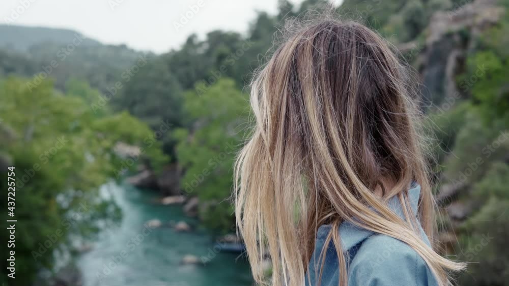 Side view of woman tourist walks by the road bridge with view of green hills and river Side view of woman tourist walks by the road bridge with view of green hills and river