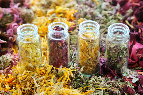 Glass bottles of medicinal herbs - helichrysum, rose petals, calendula, wild marjoram. Dry plants, herbs and flowers on table. Alternative medicine. photo