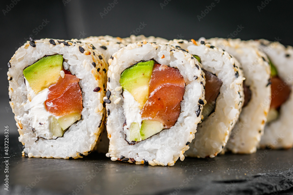 appetizing california sushi roll with cheese avocado cucumber and salmon in sesame seeds on a black stone plate appetizing california sushi roll with cheese avocado cucumber and salmon in sesame seeds on a black stone plate