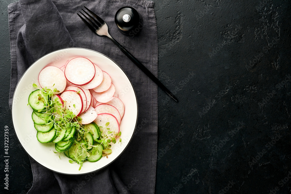 Fresh salad with red radish, cucumber, vegetables, microgreen radishes in white plate on grey stone background. View from above. Concept vegan and healthy eating.