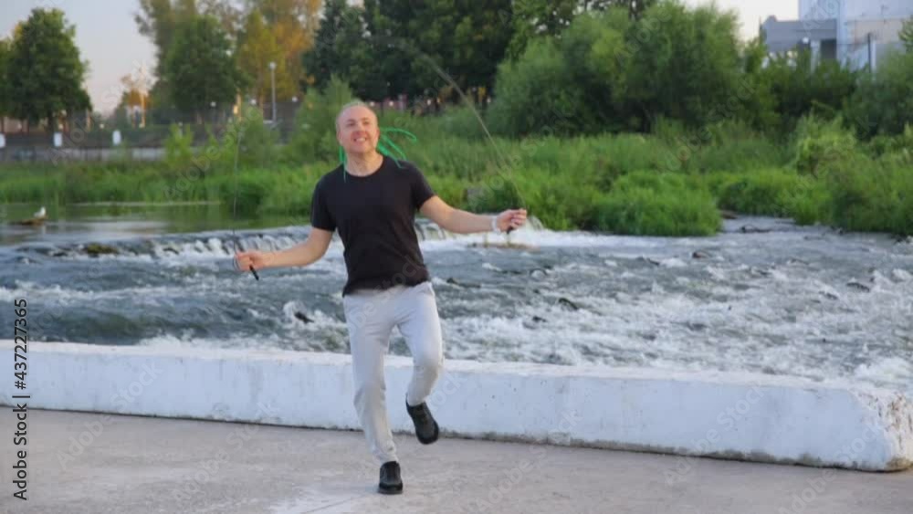 Young attractive man with braided hairstyle jumping rope against the background of the river. Young attractive man with braided hairstyle jumping rope against the background of the river.