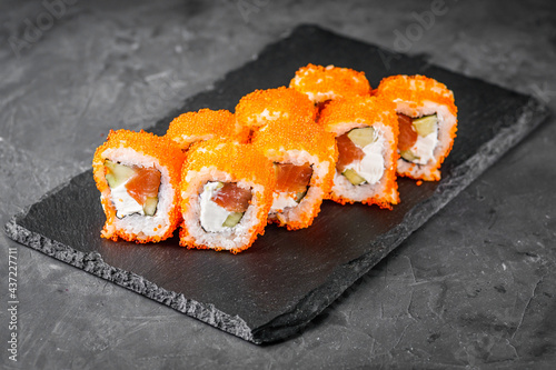 appetizing sushi roll california with salmon cucumber cheese and masago caviar on a black stone plate