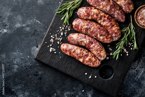 Raw sausages or bratwurst on cutting board with spices and ingredients for cooking. Top view with copy space on stone table.