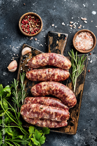Raw sausages or bratwurst on cutting board with spices and ingredients for cooking. Top view with copy space on stone table.