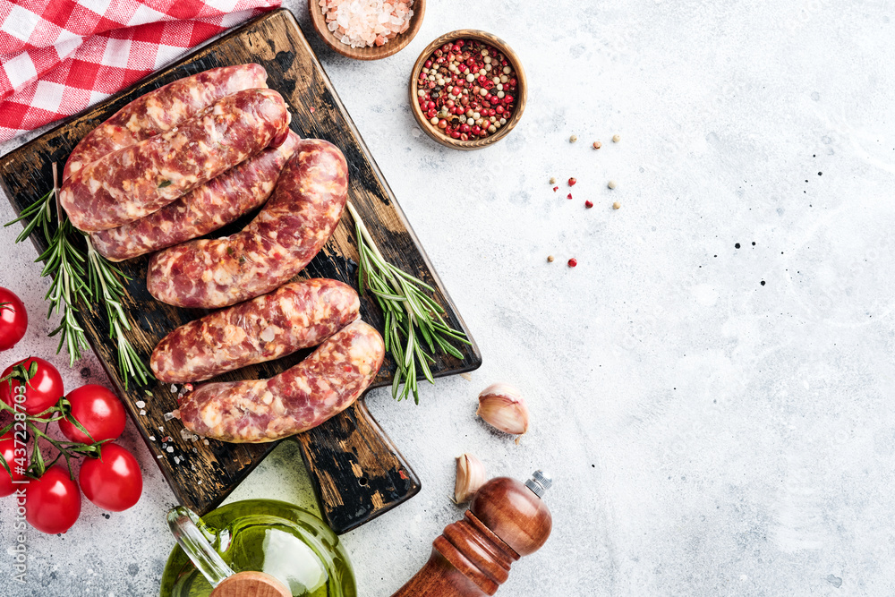 Raw sausages or bratwurst on cutting board with spices and ingredients for cooking. Top view with copy space on light grey stone table. Raw sausages or bratwurst on cutting board with spices and ingredients for cooking. Top view with copy space on light grey stone table.